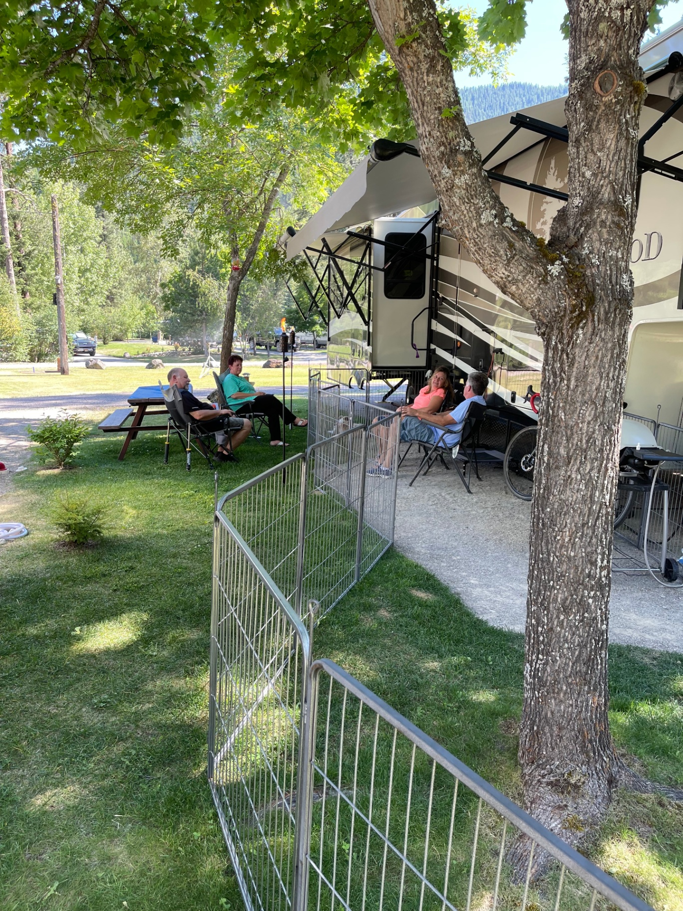 Guests relaxing in camp chairs beside their RV under shade trees at Campground St. Regis